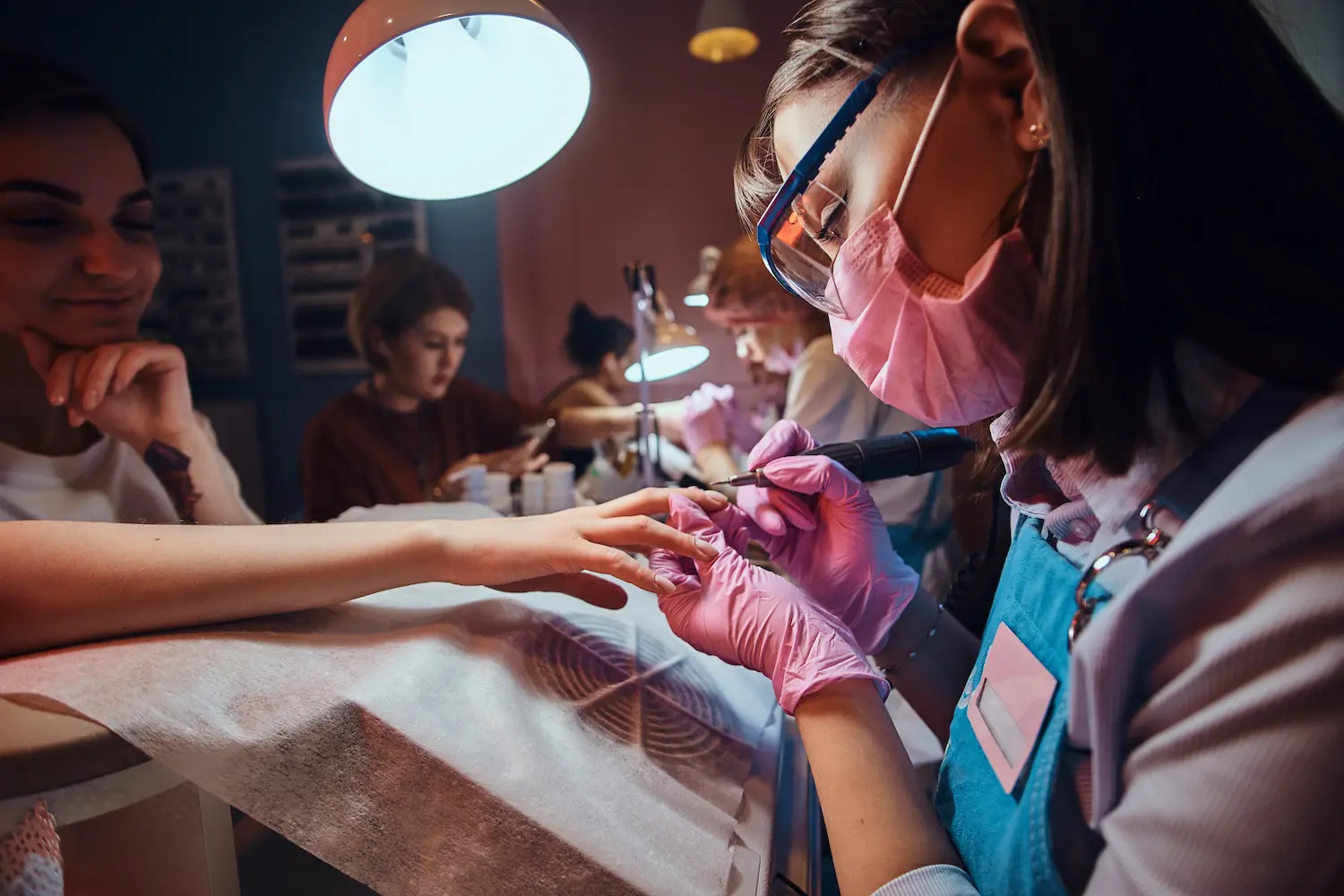 Nail technician using electric drill for manicure, wearing blue gloves. Nail technician using electric drill for manicure, wearing blue gloves.